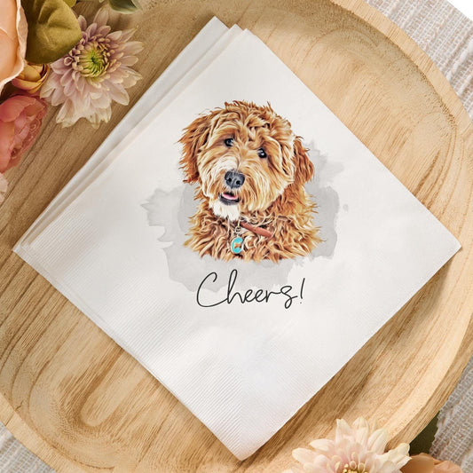 Custom white cocktail napkin featuring a watercolor illustration of a curly-haired dog with a blue tag and the text 'Cheers!' displayed on a wooden tray with pastel flowers, perfect for pet-themed weddings or special events.