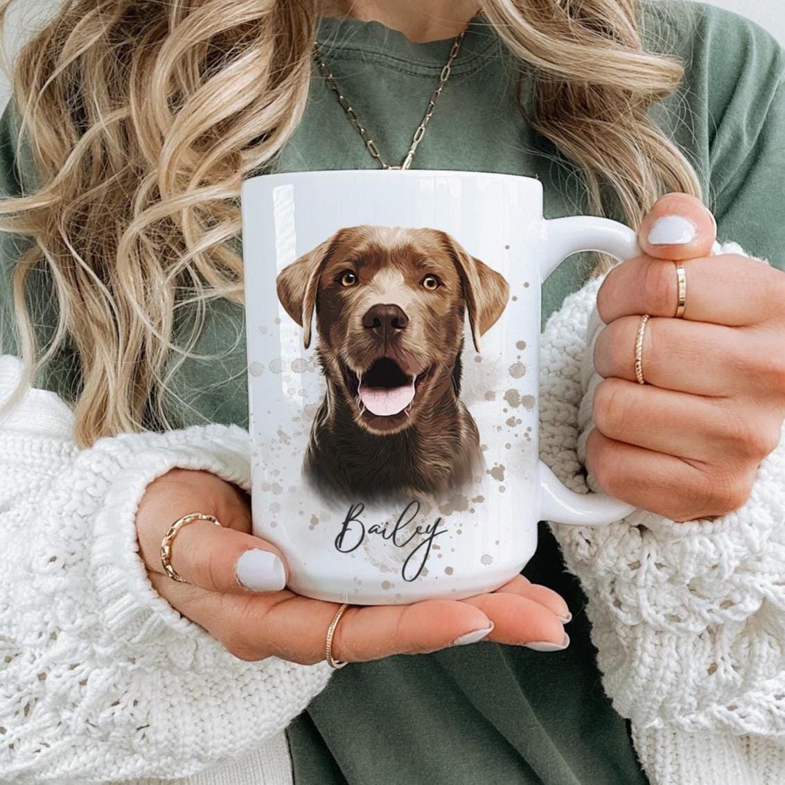 Personalized dog portrait mug being held by woman, custom white coffee cup with watercolor style brown Labrador illustration and name Bailey, cozy neutral sweater and casual outfit background