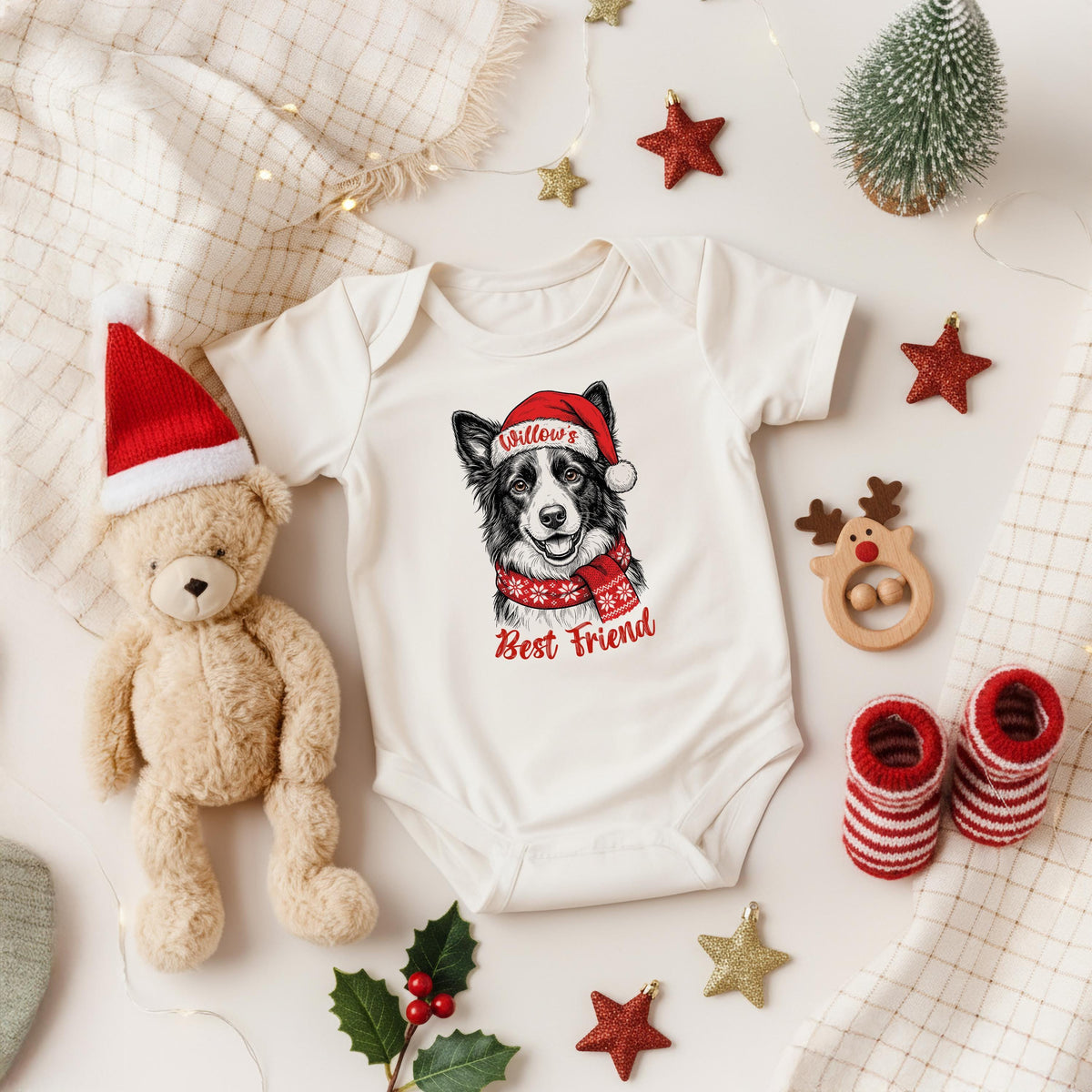A white onesie with a dog wearing a Santa hat, a teddy bear, Christmas decorations, and a pair of red and white striped socks are arranged on a white background.