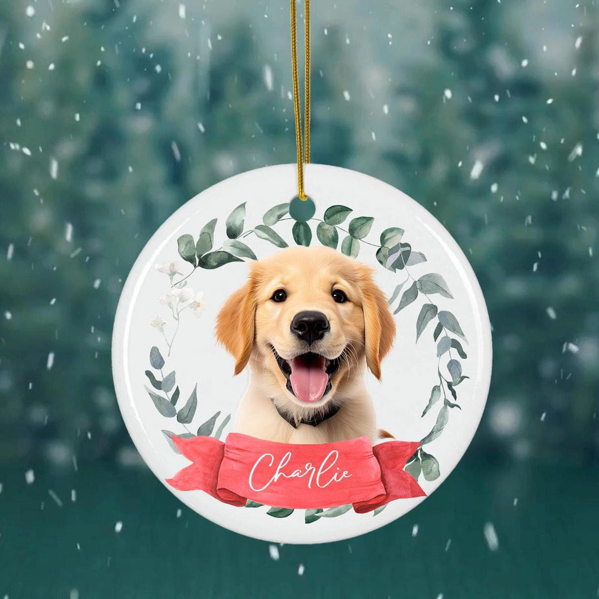 Custom holiday ornament depicting a golden retriever surrounded by eucalyptus and a red ribbon banner, displayed against a snowy winter backdrop.