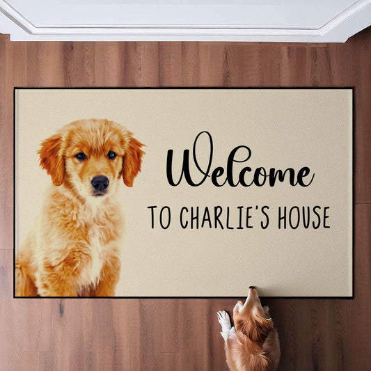 Custom pet doormat featuring an adorable golden retriever puppy with text reading 'Welcome to Charlie's House,' placed on a wooden floor with a dog looking at it, designed for personalized home entry décor.