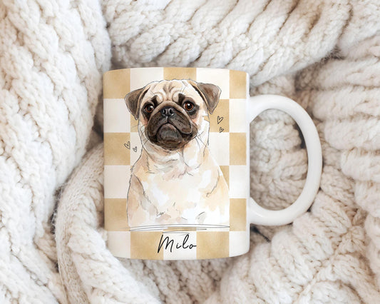 Personalized watercolor pug dog portrait mug with beige checkered pattern, featuring a custom watercolor pet illustration and name on ceramic coffee cup, styled on a cozy knit blanket, custom pet gift for dog lovers.